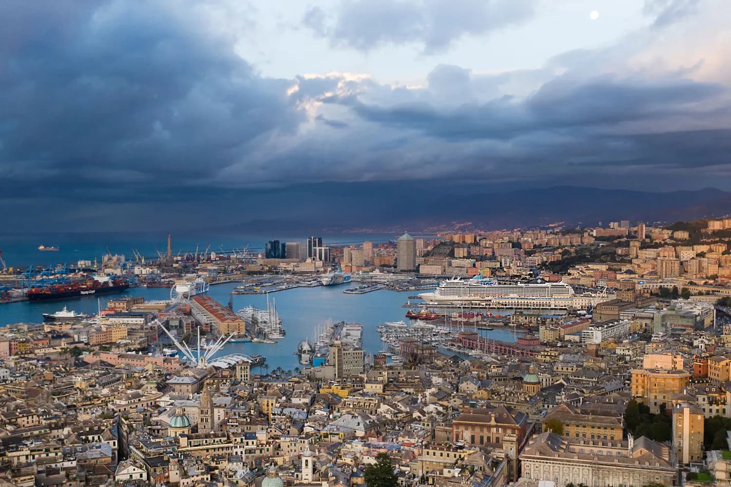 Luftaufnahme von Genua mit Hafengebiet, Kreuzfahrtschiff, Containerterminal und Stadtbebauung unter bewölktem Himmel