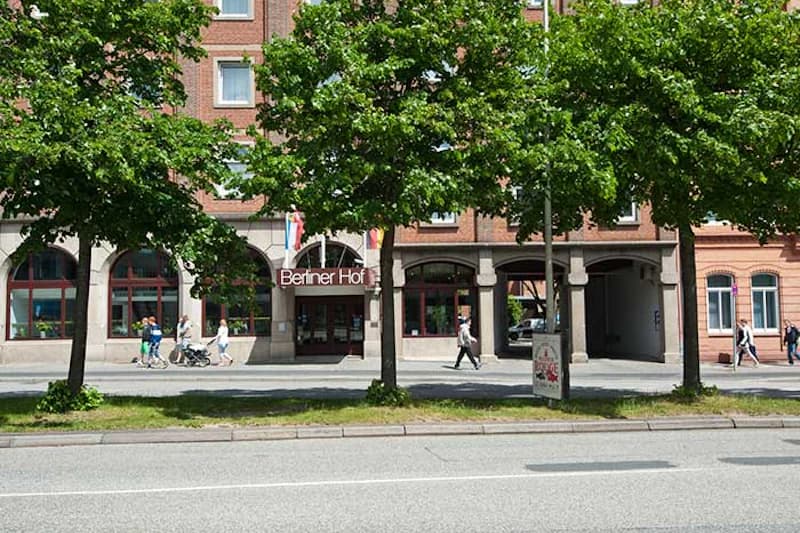 Fassade des Berliner Hof Kiel mit Eingangsportal, Bäumen vor dem Gehweg und Passanten.